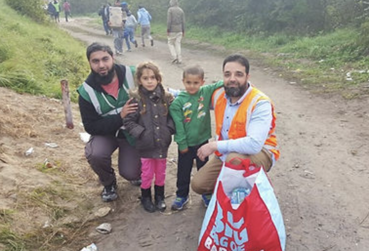 Two men posed with their arms around two young children outdoors.